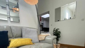 A modern living room with a grey sofa, a floor lamp, a glass of wine, and a large mirror on the wall.
