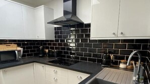 A modern kitchen with white cabinets, black tiled backsplash, stainless steel appliances, and a black countertop.