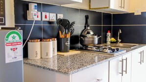 Una cocina con encimeras de granito, armarios blancos y un salpicadero negro. Se observan tres recipientes etiquetados con azúcar, té y café. Hay una estufa y un fregadero a la vista, junto con un juego de cuchillos y una olla sobre la encimera.