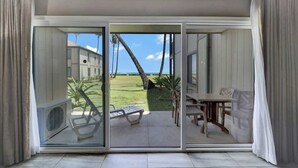 A room with a sliding glass door leading to an outdoor area with a table and chairs, a bench, and a view of the ocean.