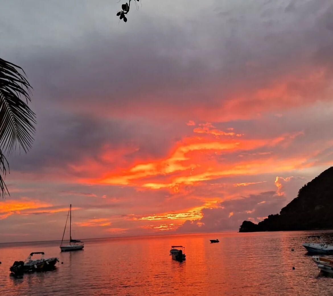 Un coucher de soleil sur une mer calme, avec des bateaux et une côte montagneuse.