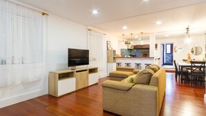 A modern living room with a flat-screen TV, a sofa, and a dining area with a kitchen in the background.