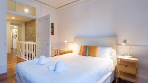 A hotel room with a large bed, a wooden nightstand, a desk, and a view of the hallway.
