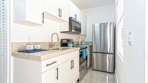 Eine kompakte Küche mit weißen Schränken, Edelstahlgeräten, einer Mikrowelle, einem Backofen und einem Kühlschrank.