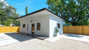 Ein kleines, eingeschossiges Gebäude mit weißer Fassade und dunklem Dach. Es besitzt eine Eingangstür, zwei Fenster und eine kleine Veranda.