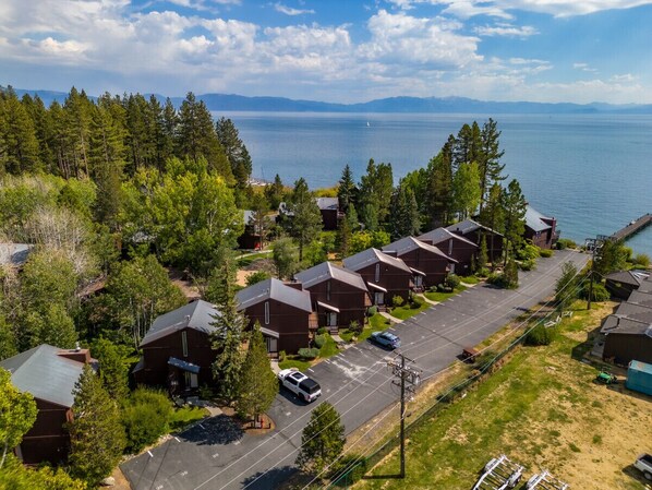A residential area with houses along a street, a dock extending into a large body of water, and a mountainous backdrop.
