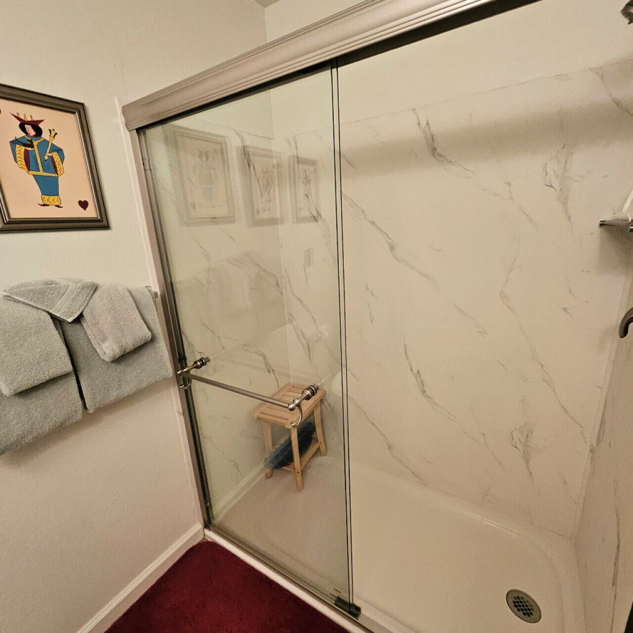 Ein Badezimmer mit Duschabtrennung aus Glas, einem hölzernen Hocker und einem Handtuchhalter mit Handtüchern.