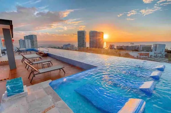 Piscina infinita no terraço com vista para a cidade ao pôr do sol.