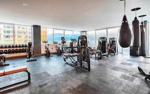 Academia com diversos equipamentos de exercício, janelas amplas e vista para montanhas.
