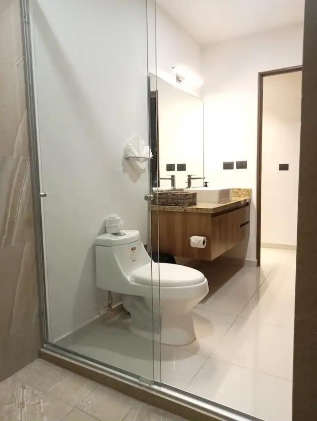 A modern bathroom with a glass-enclosed shower, a toilet, and a vanity with a mirror.