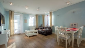A living room with a sofa, coffee table, dining table with chairs, and a TV. - Nautica by Grand Apartments (Sopot)