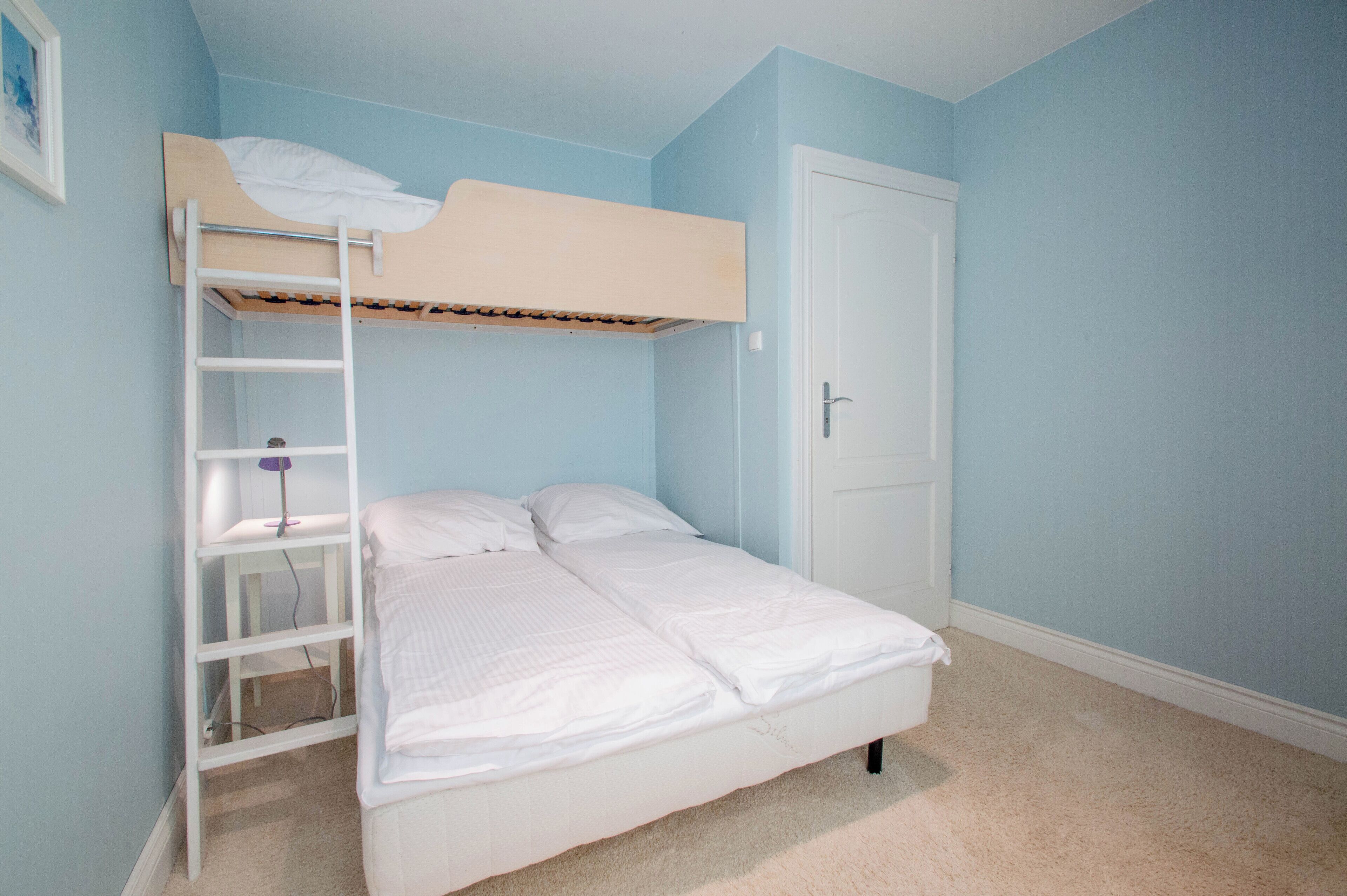Un lit superposé avec une échelle, une porte blanche et un mur bleu clair.