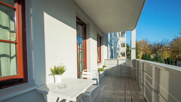 A balcony with a white table and chairs, potted plants, and a view of trees and buildings. - Nautica by Grand Apartments (Sopot)
