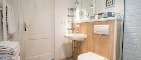 A bathroom with a white door, a sink, a toilet, and a towel rack with folded towels.