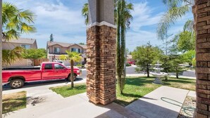 A residential street with a red pickup truck parked on the side, a stone pillar, and a well-maintained lawn with a small statue.