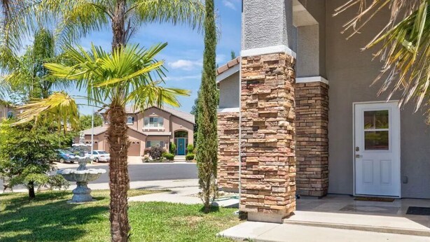 A residential house with a stone facade, a front door, and a well-maintained lawn with palm trees.