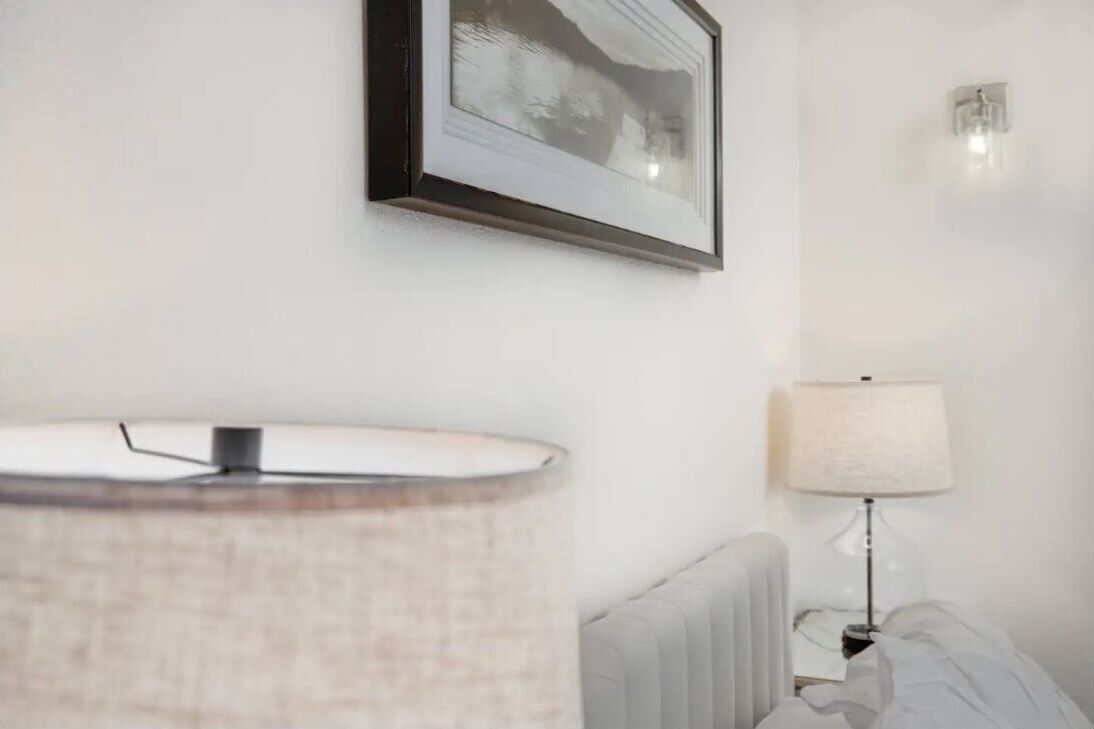 A hotel room with a bed, a bedside table with a lamp, a framed picture on the wall, and a radiator.