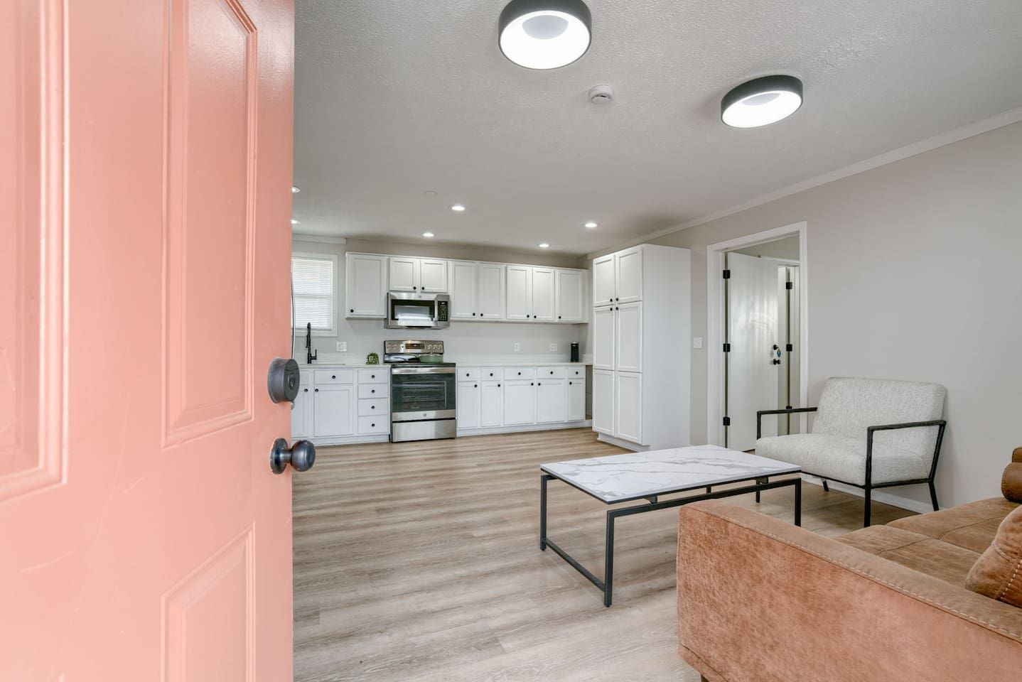 A modern kitchen with white cabinets, stainless steel appliances, and a wooden floor.
