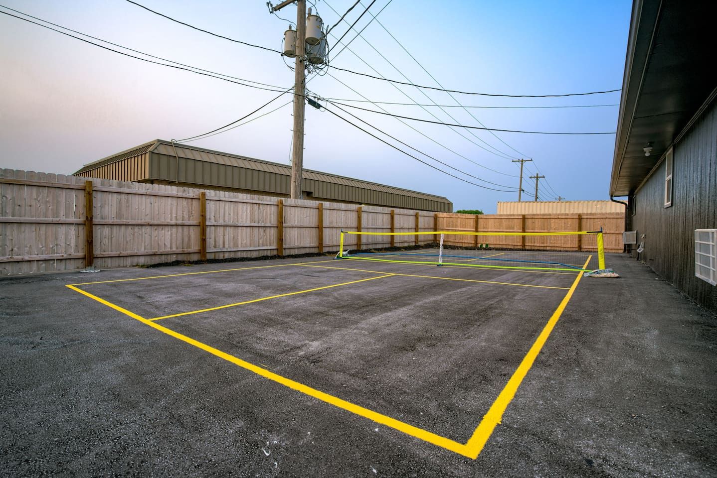 A parking lot with yellow lines marking spaces, a wooden fence, and a building with a metal roof.