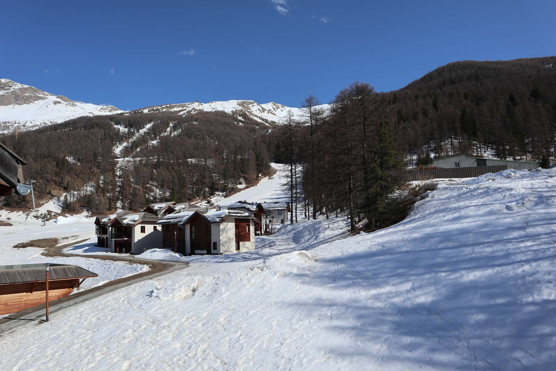 Un paysage de montagne enneigé, avec un chalet comprenant plusieurs bâtiments et une piste de ski.