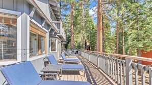 Une terrasse dotée de chaises longues et de tables, entourée de grands arbres.