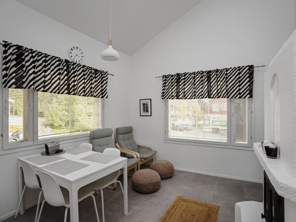 A modern, well-lit room with a dining table, two chairs, a sofa, and a fireplace.