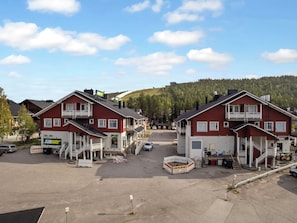 Et hotel med to røde bygninger, en parkeringsplads og en skovklædt bakke i baggrunden.