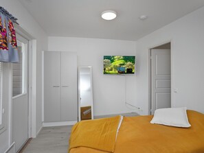 Et soveværelse med en seng, et fjernsyn ophængt på væggen og et klædeskab.