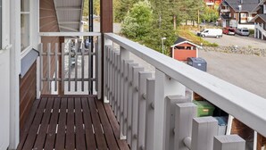 A wooden deck with a white railing, overlooking a parking area and buildings in the background. - Leviraitti 4 a 4 by Interhome (Kittilä)