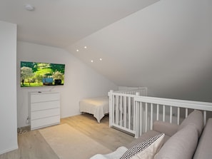 A modern, well-lit room with a white crib, a sofa, and a flat-screen TV mounted on the wall. - Leviraitti 4 a 4 by Interhome (Kittilä)
