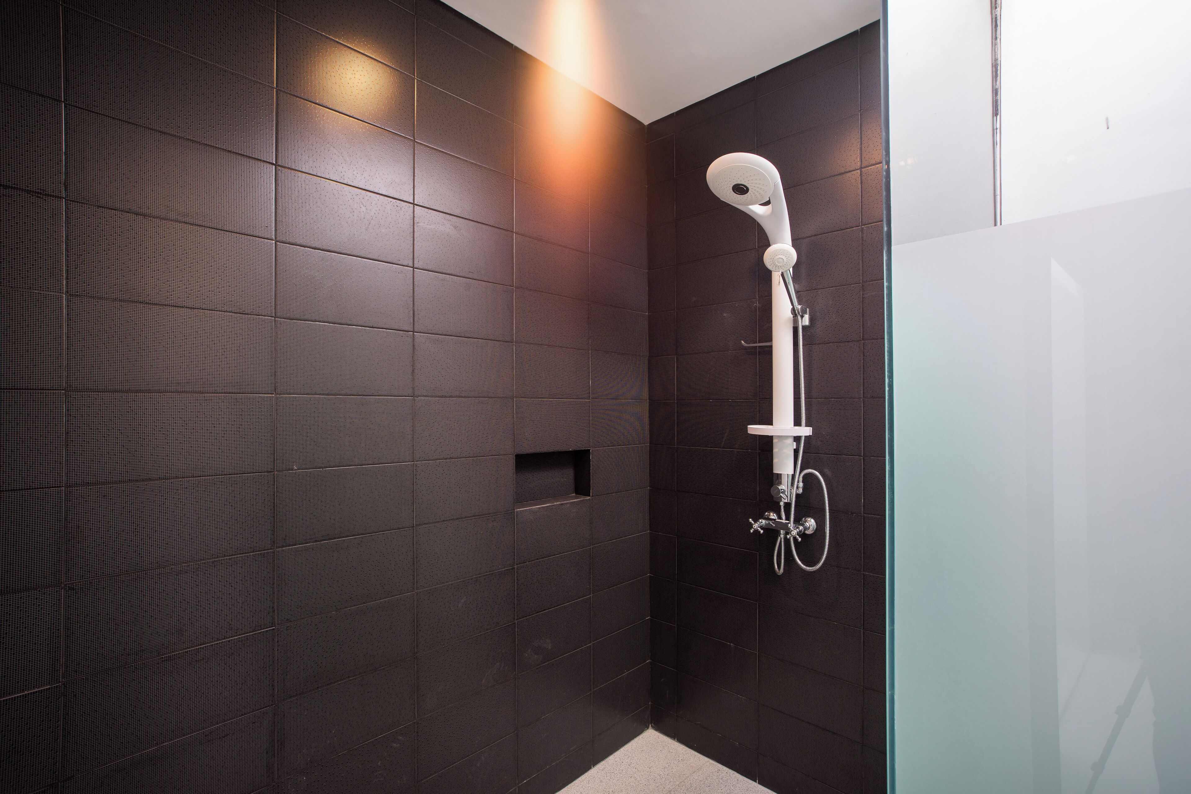 Une douche moderne dotée d’un pommeau de douche à main, de murs recouverts de carreaux sombres et d’une petite fenêtre.