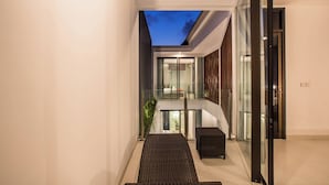 A modern interior with a glass door leading to a balcony, a wicker bench, and a staircase. - Berawa Bali Beach Villa (Canggu)