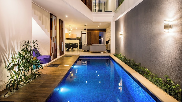 A modern indoor pool area with a clear view of the adjacent living space, including a staircase and seating area. - Berawa Bali Beach Villa (Canggu)