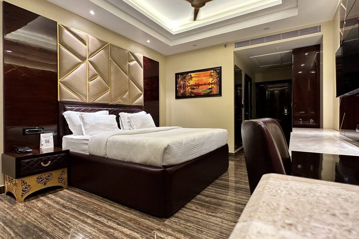 Quarto de hotel com uma cama grande, uma mesa e uma cadeira. Há um ventilador de teto e um quadro na parede.