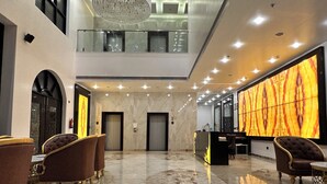 A spacious lobby with marble flooring, a reception desk, and two elevators.