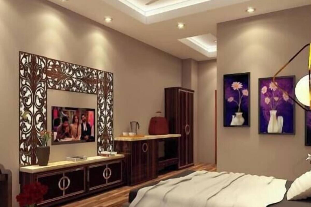 Quarto moderno com cama, TV, espelho decorativo e obras de arte nas paredes.