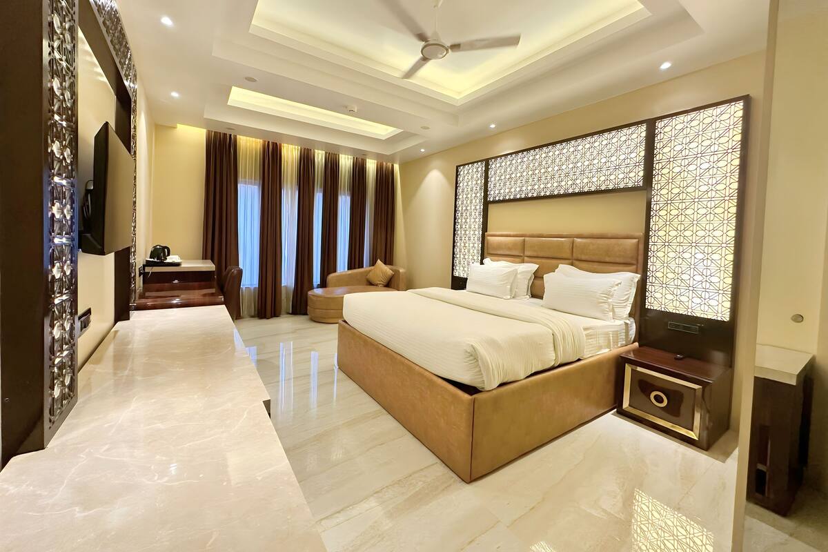 Quarto de hotel moderno com uma cama grande, área de estar, televisão de tela plana e ventilador de teto.