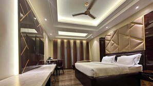 A modern hotel room with a large bed, a desk, and a chair. There is a ceiling fan and recessed lighting.