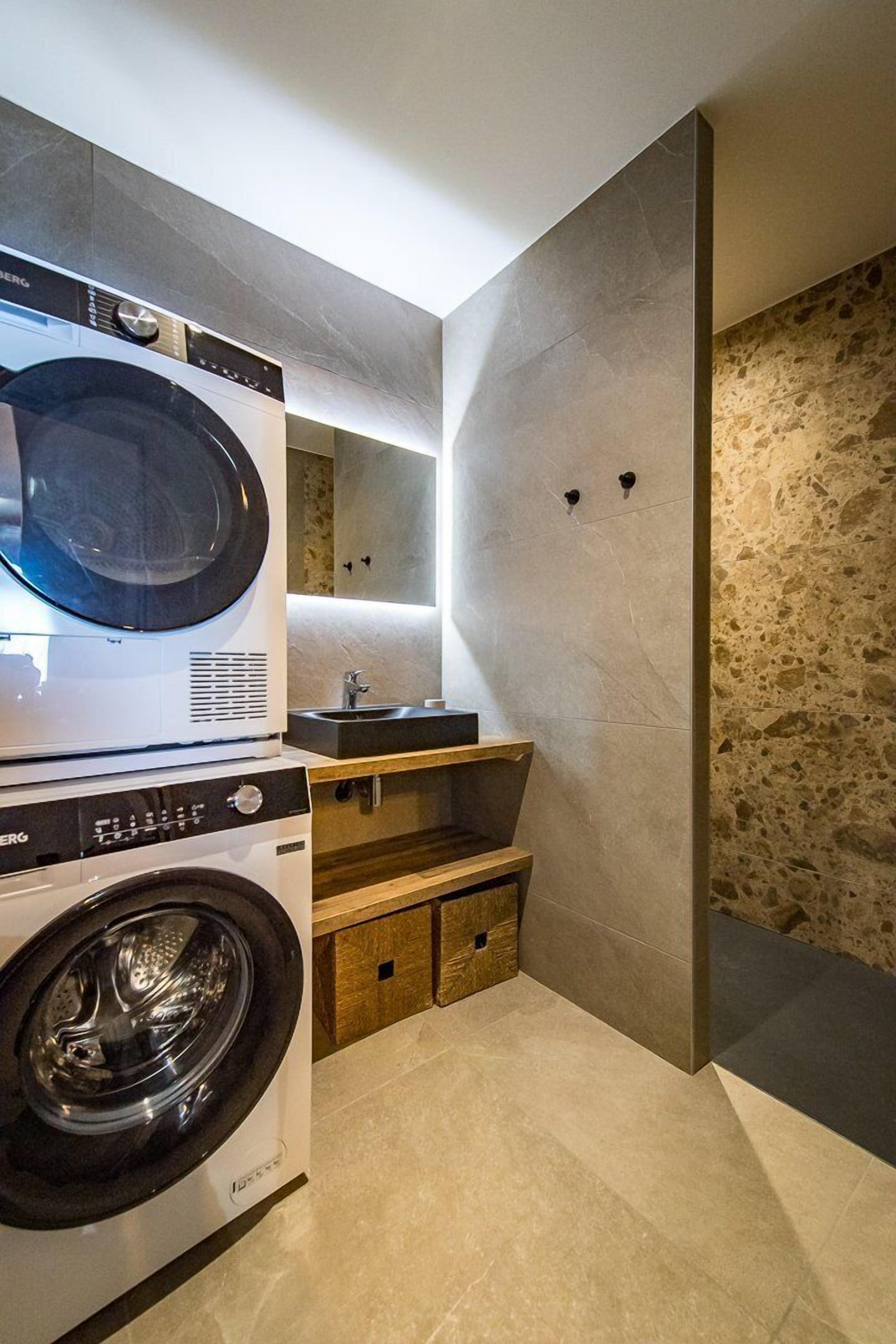 A modern laundry room with a front-loading washing machine and dryer, a sink, and a wooden cabinet.