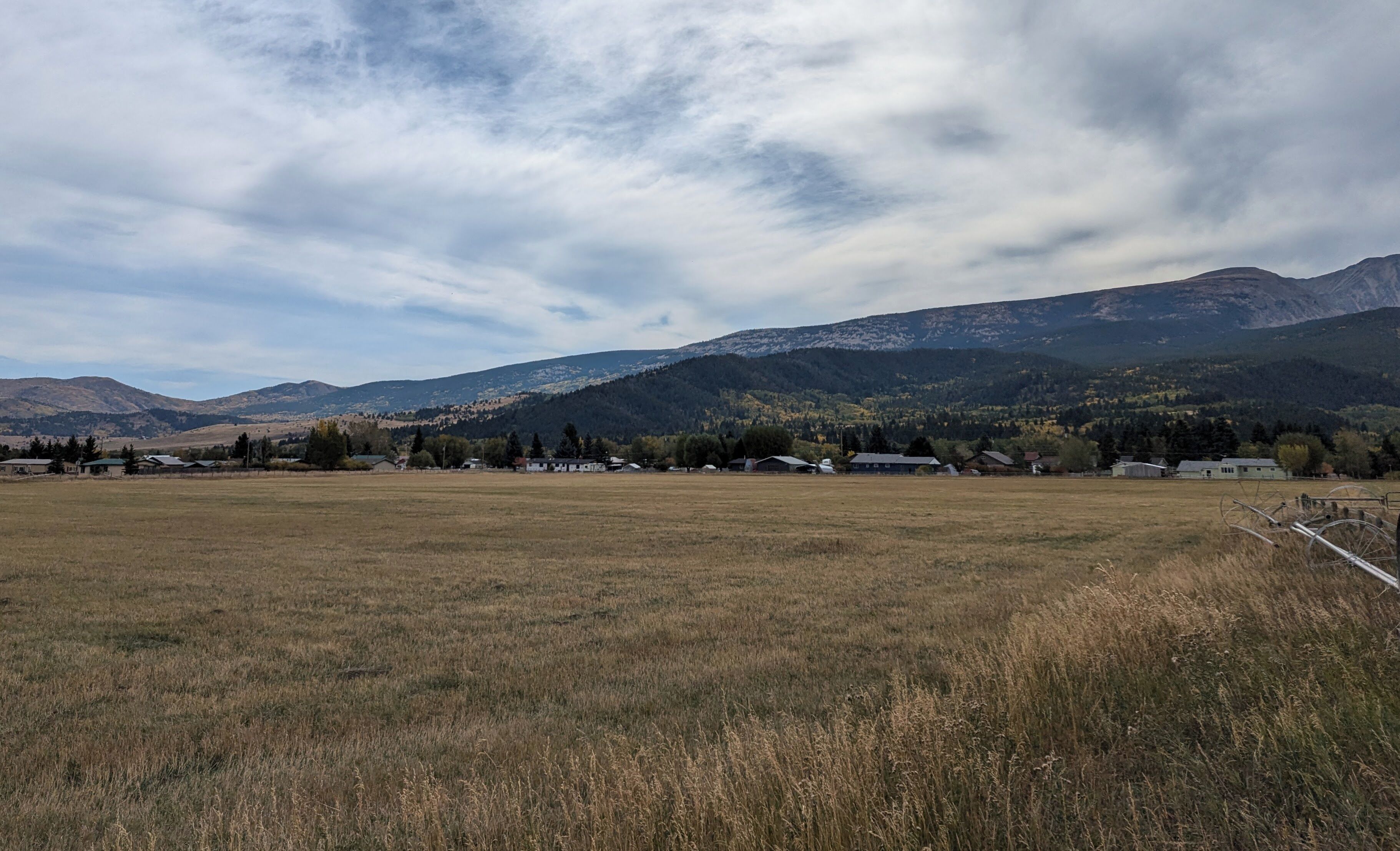 Un paysage rural avec un champ, quelques bâtiments dispersés et des montagnes en arrière-plan.