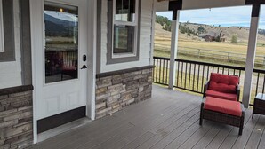A covered porch with a stone wall, a wooden deck, and a red cushioned chair. - Family-Friendly Private Ranch Getaway with pond. Newly Remodeled (Anaconda)