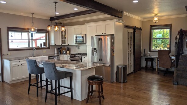 A modern kitchen with white cabinets, a central island with bar stools, stainless steel appliances, and pendant lighting. - Family-Friendly Private Ranch Getaway with pond. Newly Remodeled (Anaconda)