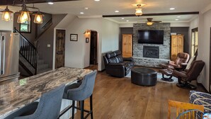 A spacious living area with a stone fireplace, leather seating, and a large TV mounted on the wall. - Family-Friendly Private Ranch Getaway with pond. Newly Remodeled (Anaconda)