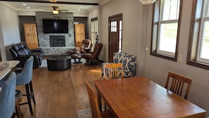 A spacious living room with a stone fireplace, leather seating, a dining table, and large windows. - Family-Friendly Private Ranch Getaway with pond. Newly Remodeled (Anaconda)