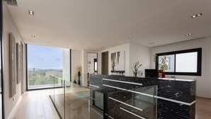 A modern kitchen with a black marble island, glass railings, and large windows offering a view of the outdoors. - Modern 4 bedroom villa with pool and barbecue (Llubi)