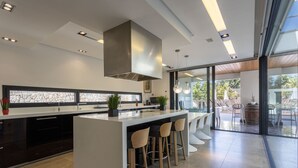 A modern kitchen with a central island, bar stools, and a large window overlooking a patio area. - Modern 4 bedroom villa with pool and barbecue (Llubi)