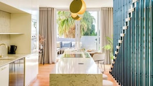 A modern kitchen with a marble countertop, a dining area with a white table, and a view of greenery outside. - Ultimate Escape in Vibrant De Waterkant at Ishani (Cape Town)