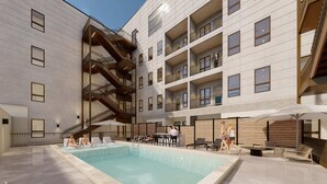 Un bâtiment moderne doté d’un espace piscine, comprenant un balcon à plusieurs niveaux, des espaces de détente en plein air et un bar.