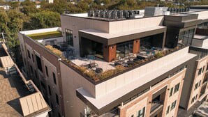 Un bâtiment moderne doté d’une terrasse sur le toit, comprenant un espace extérieur aménagé avec des sièges et un jardin.