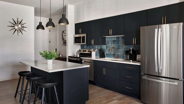 Une cuisine moderne avec des meubles de couleur sombre, des appareils en acier inoxydable et un îlot central doté de tabourets.